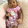 baby, infant, pink_clothing, hello_kitty, cushion, soft_texture, smiling, portrait, child, cute, comfortable, indoors, closeup, baby_girl, apparel, seated, happy, skin, face, hand