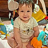 baby, child, smiling, play_mat, toys, plush_toy, colorful, indoor, cute, happy, sitting, person, infant, clothing, face, soft, developmental_toys, playtime, baby_gym, bright