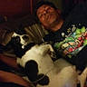 animal, bed, black_and_white_dog, blanket, candid, casual, comfort, companion, dim_lighting, dog, home, indoor, lying_down, man, person, pet, relaxed, resting, sleepy, tshirt