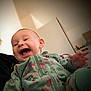 baby, child, smiling, laughing, onesie, floral_pattern, green_clothing, indoor, person, face, hand, infant, happiness, joy, cute, portrait, soft_light, warm_tones, blurred_background, cozy