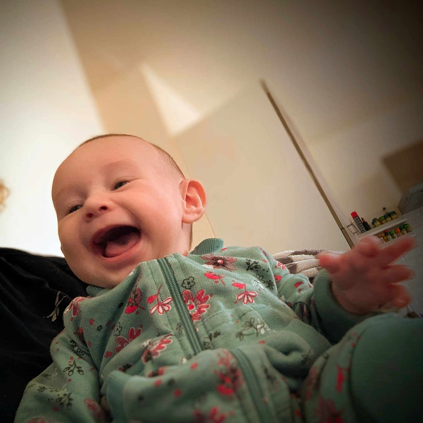 Héloïse a rejoint le concours — aidez-le/la à gagner de superbes lots ! baby, blurred_background, child, cozy, cute, face, floral_pattern, green_clothing, hand, happiness, indoor, infant, joy, laughing, onesie, person, portrait, smiling, soft_light, warm_tones