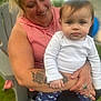 woman, baby, child, smiling, holding, outdoor, grass, chair, tattoo, ring, hoodie, long_sleeve, pants, rainbow_pattern, face, person, happy, closeup, nature, family