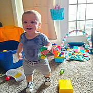 Jaxton is registered to the contest to win money with this photo: toddler, child, toy, indoor, carpet, playroom, window, clothing, shorts, shirt, footwear, sneakers, smiling, happy, person, young_child, play, colorful, daylight, home
