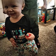 Jaxton joined the competition — help win amazing prizes! child, baby, toddler, smile, face, standing, birthday_shirt, clothing, patterned_pants, toy, carpet, indoor, home, playroom, adult_legs, hand, candid, closeup, happy, floor