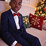 bow_tie, boy, celebration, child, christmas_tree, couch, festive, formal_wear, holiday, holiday_decorations, home, indoors, lights, pillow, portrait, seasonal, smiling, suit, window, young