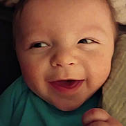 August is registered to the contest to win money with this photo: baby, face, smile, blue_shirt, koala_print, hand, closeup, infant, cute, cheek, eyelids, skin, expression, portrait, indoors, soft_light, cozy, young_child, person, happy