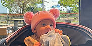 Lyana a rejoint le concours — aidez-le/la à gagner de superbes lots ! baby, blanket, cars, chewing, child, clothing, comfort, cute, daylight, face, indoor, infant, person, pink_hat, pom_poms, seated, soft_toy, stroller, trees, window