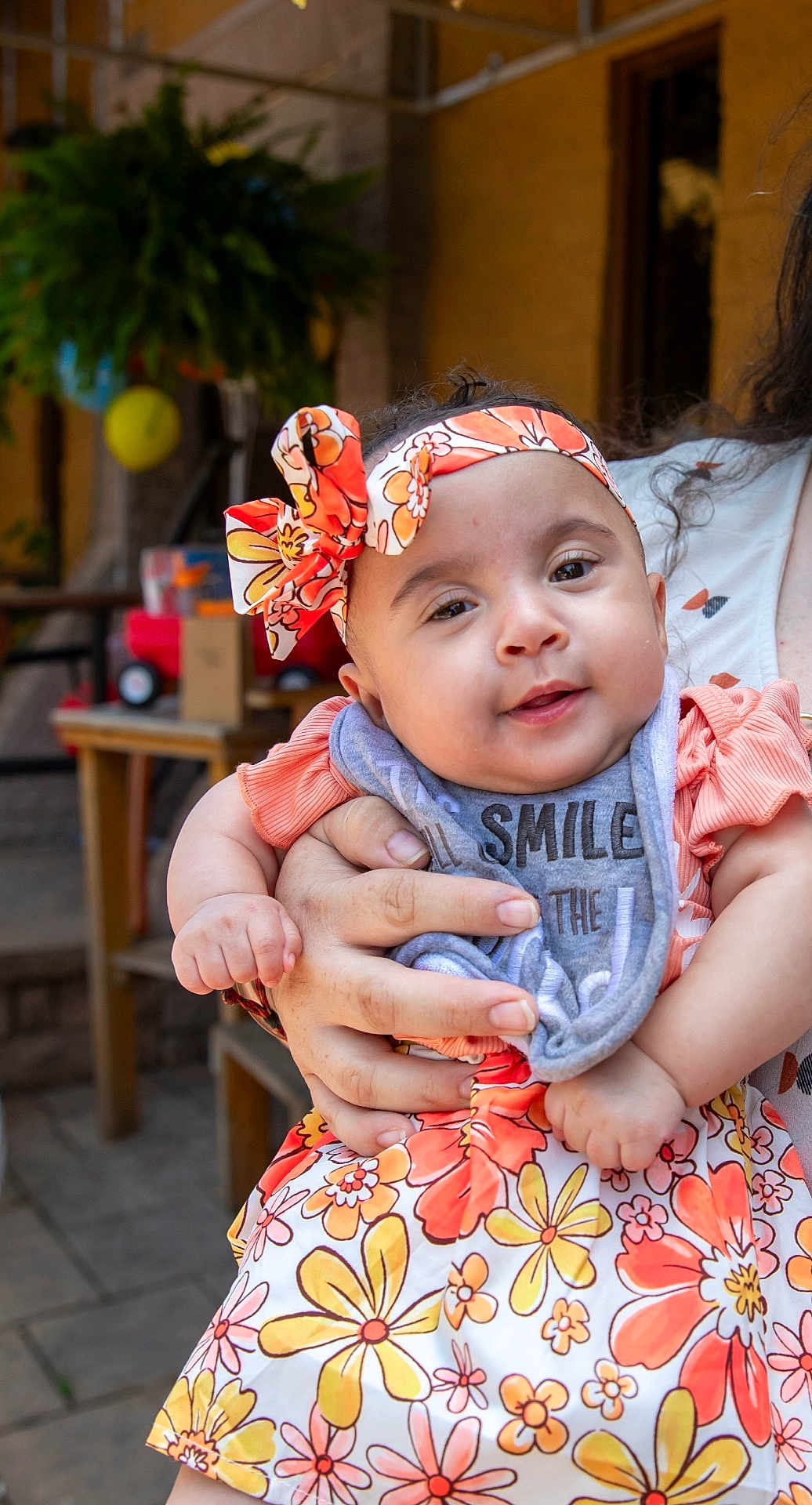 Ka'Lia joined the competition — help win amazing prizes! baby, child, smile, headband, floral_dress, bib, hand, person, outdoor, background, greenery, table, chair, holding, cute, portrait, infant, colorful, happy, warm