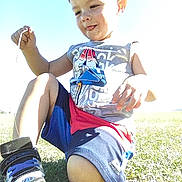 Damon is registered to the contest to win money with this photo: child, boy, outdoor, grass, sunlight, sitting, shorts, tshirt, shoe, playful, tongue_out, casual_clothing, summer, nature, daylight, cute, young, fun, person, kneeling