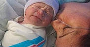 Dakota joined the competition — help win amazing prizes! adult, affection, baby, bed, blanket, care, closeup, face, glasses, hospital, hospital_gown, human, infant, kiss, medical, newborn, parent, person, surgical_cap, swaddled