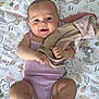 baby, barefoot, blanket, child, clothing, cute, face, floor, happy, indoors, infant, lying_down, pattern, person, playful, skin, sleeveless, smiling, soft_toy, young