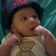 Xavier joined the competition — help win amazing prizes! baby, infant, child, hat, navy_blue, onesie, teddy_bear, text, cute, hand, fingers, lying_down, blue_background, clothing, portrait, face, expression, young, adorable, indoor