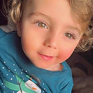 Mahmoud is registered to the contest to win money with this photo: child, toddler, curly_hair, blonde, brown_eyes, smile, blue_shirt, snowman_print, cozy_clothing, portrait, closeup, indoor, soft_light, rosy_cheeks, cute, young_child, casual_wear, happy, face, person
