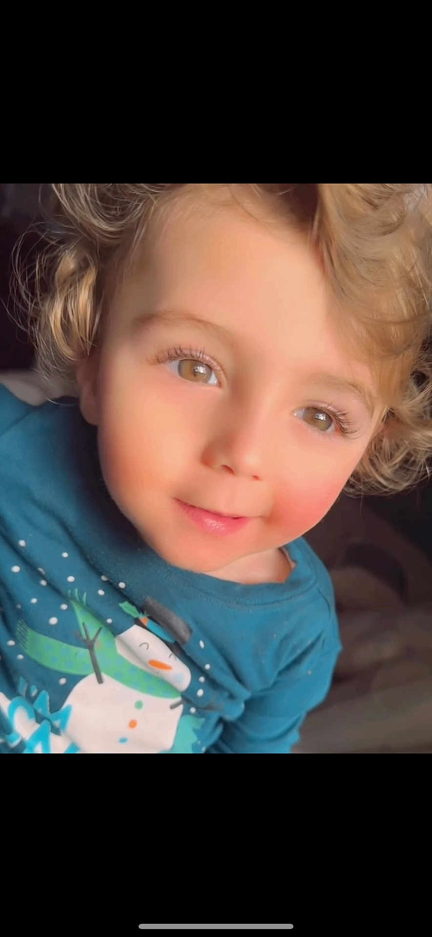 Mahmoud is registered to the contest to win money with this photo: child, toddler, curly_hair, blonde, brown_eyes, smile, blue_shirt, snowman_print, cozy_clothing, portrait, closeup, indoor, soft_light, rosy_cheeks, cute, young_child, casual_wear, happy, face, person