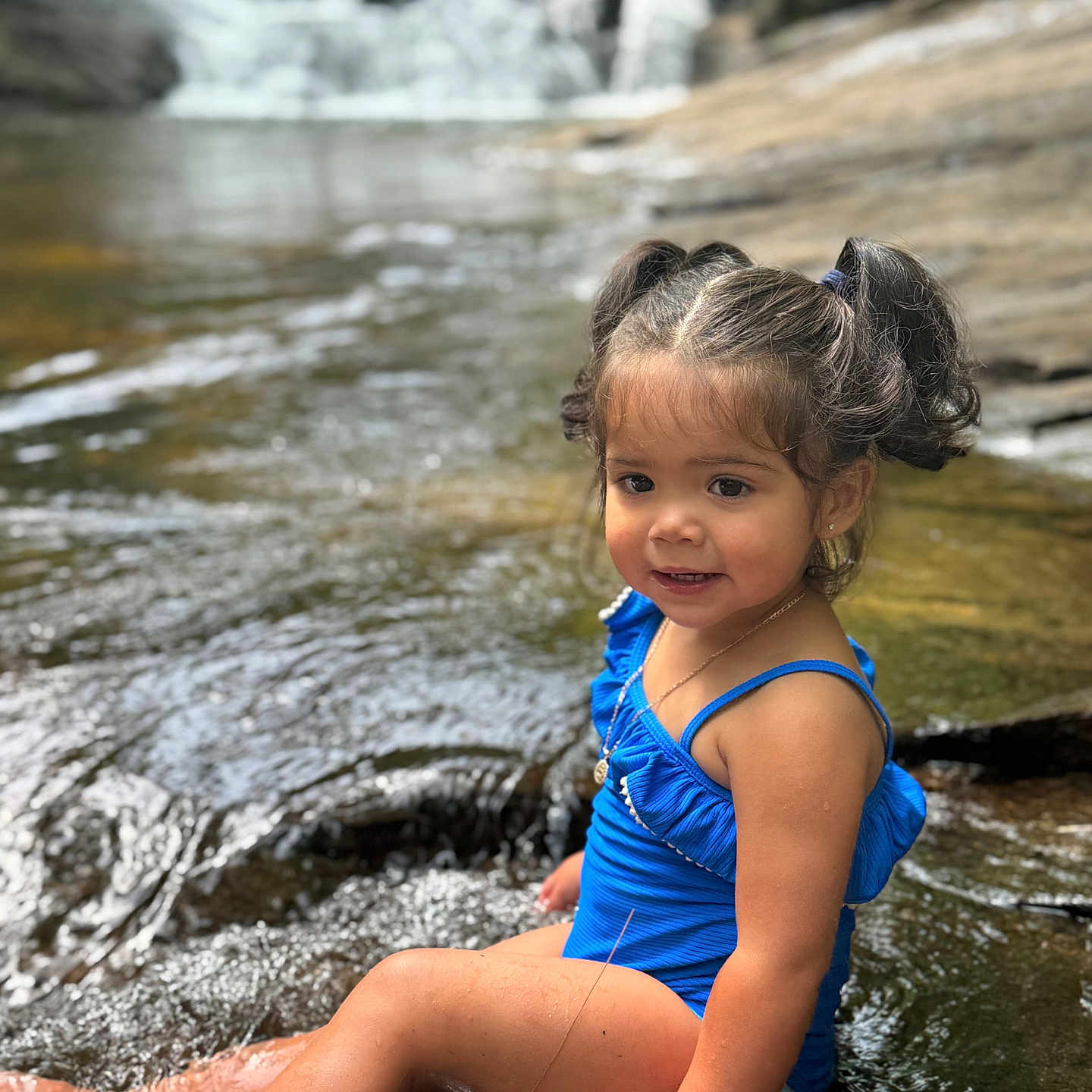 Jazmynn joined the competition — help win amazing prizes! blue, child, girl, happy, nature, necklace, outdoor, pigtails, play, portrait, rocks, sitting, smiling, stream, summer, sunlight, swimsuit, toddler, water, waterfall