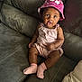 baby, bucket_hat, casual_clothing, child, comfortable, couch, curious_expression, cute, floral_hat, gray_couch, home, indoors, infant, open_mouth, pink_outfit, pink_socks, portrait, seated, wide_eyes, young_child