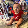 baby, child, red_onesie, holiday_decorations, nutcracker, snowman, floor, wooden_floor, festive, curious_expression, sitting, indoor, decor, toy, christmas, cute, face, person, holiday, winter
