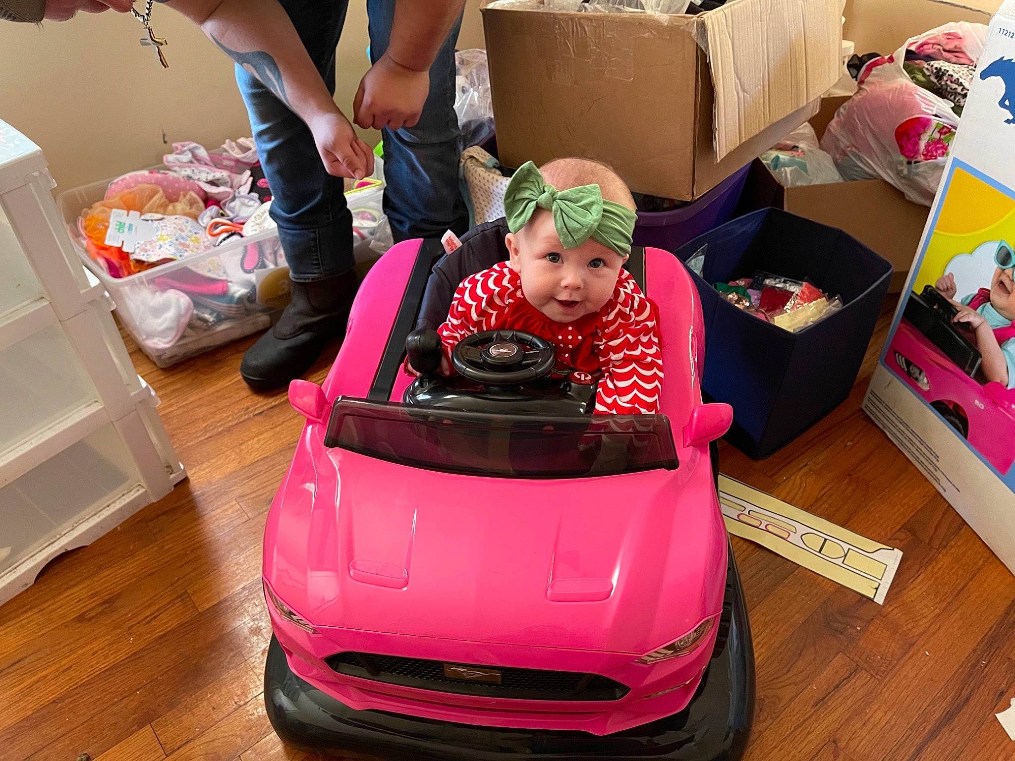 Harmonie is registered to the contest to win money with this photo: automotive_design, automotive_exterior, box, bumper, cardboard, child, floor, flooring, grille, hardwood, headwear, hood, laminate_flooring, person, pink, riding_toy, shipping_box, shoe, toddler, toy_vehicle