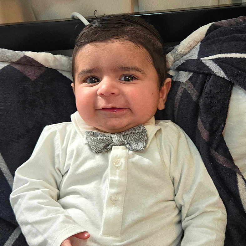 Sahai is registered to the contest to win money with this photo: accessories, baby, clothing, coat, couch, cushion, face, formalwear, happy, head, homedecor, jacket, pants, person, photography, portrait, shirt, sitting, smile, tie