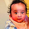 baby, child, curly_hair, bib, striped_shirt, tattoo, arm, face, rosy_cheeks, wide_eyes, indoor, person, portrait, holding, cute, expression, infant, skin, clothing, background
