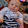 baby, infant, striped_clothing, face, eyes, hand, indoor, living_room, television, toy, blanket, soft_toy, furniture, person, couch, wood_floor, child, portrait, expression, home