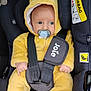 baby, car_seat, yellow_onesie, pacifier, child, infant, safety_harness, cute, indoors, seatbelt, hooded_outfit, soft_clothing, wide_eyes, car_interior, child_safety, plush, comfort, portrait, small_hands, baby_face