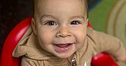 Zylan is registered to the contest to win money with this photo: child, toddler, smiling, face, eyes, hoodie, beige_clothing, red_chair, indoor, happy, baby, person, portrait, cute, seated, young_child, expression, casual_clothing, skin, hair