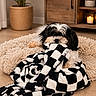 dog, black_and_white, blanket, chewing, rug, wooden_cabinet, candle, plant, potted_plant, indoor, floor, cozy, pet, fur, small_dog, home_interior, living_room, playful, animal, cute