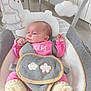 baby, infant, pink_clothing, baby_rocker, soft_toy, hanging_toy, cushion, knitted_booties, indoor, child, face, person, seat, comfort, cute, resting, newborn, baby_accessory, home, relaxation