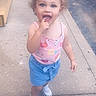 blue_shorts, car, casual_clothing, child, concrete, curly_hair, daylight, expression, finger_in_mouth, outdoor, person, pink_tank_top, playful, sidewalk, sneakers, spring, street, summer, toddler, young_child