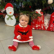 Marion a rejoint le concours — aidez-le/la à gagner de superbes lots ! baby, celebration, child, christmas_bags, christmas_tree, cute, face, festive, floor, holiday_decor, indoor, pants, person, pigtails, red_dress, seasonal, shoes, smiling, snowman_decoration, striped_leggings