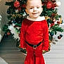child, christmas_tree, holiday, festive_clothing, red_outfit, smiling, indoors, decorations, ornaments, greenery, flooring, sneakers, happy, celebration, seasonal, holiday_spirit, young_child, portrait, christmas, tree_lights