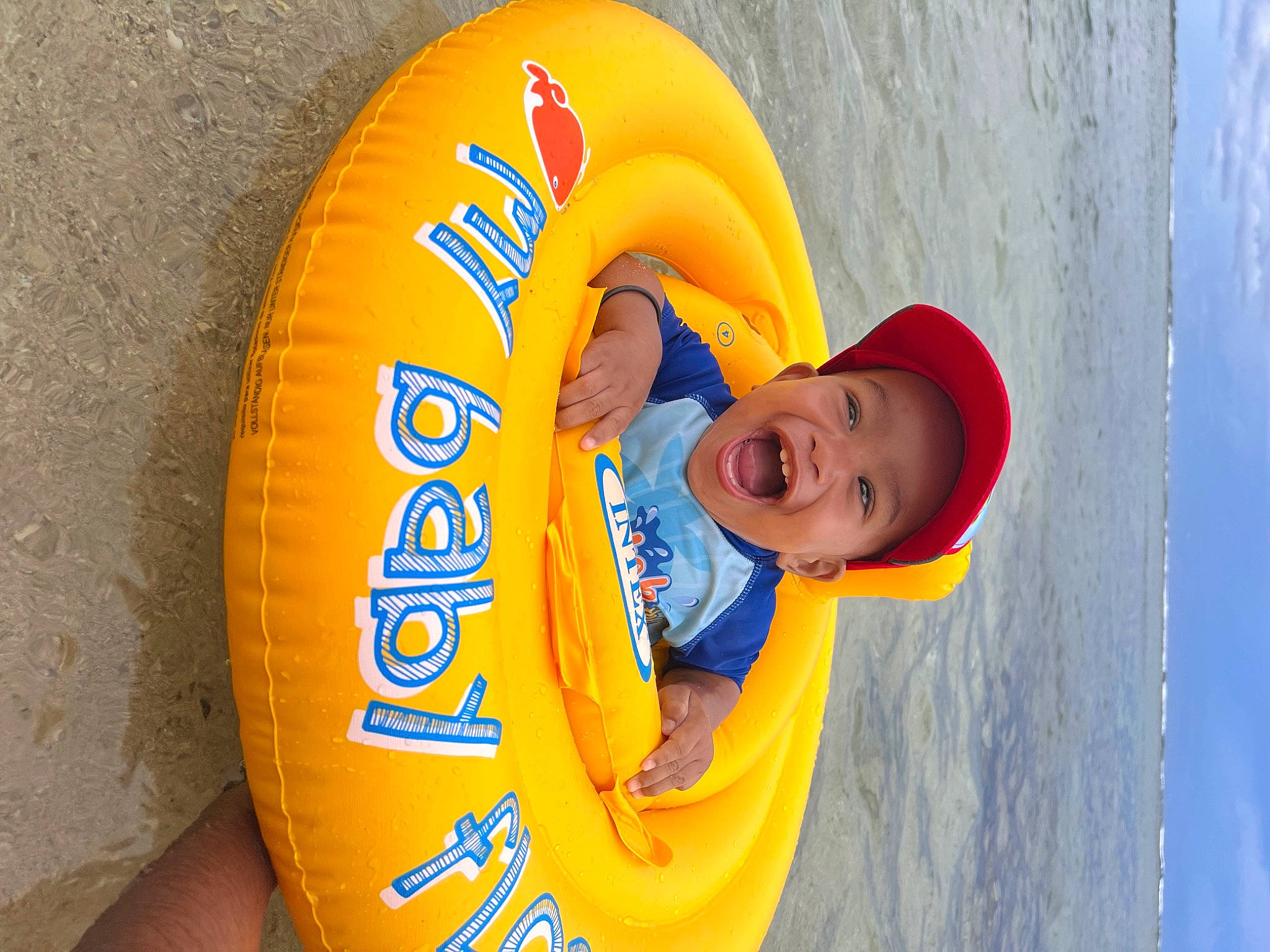 Loïc participe au concours pour gagner de l'argent avec cette photo : child, circle, electric_blue, fun, happy, hat, headgear, headwear, inflatable, leisure, lifebuoy, lifejacket, orange, person, personal_protective_equipment, recreation, smile, sun_hat, t_shirt, toddler