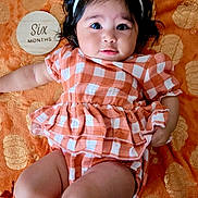 Zyla is registered to the contest to win money with this photo: baby, infant, child, girl, headband, bow, milestone, six_months, orange, checkered, outfit, socks, blanket, pattern, cute, lying_down, portrait, face, skin, expression