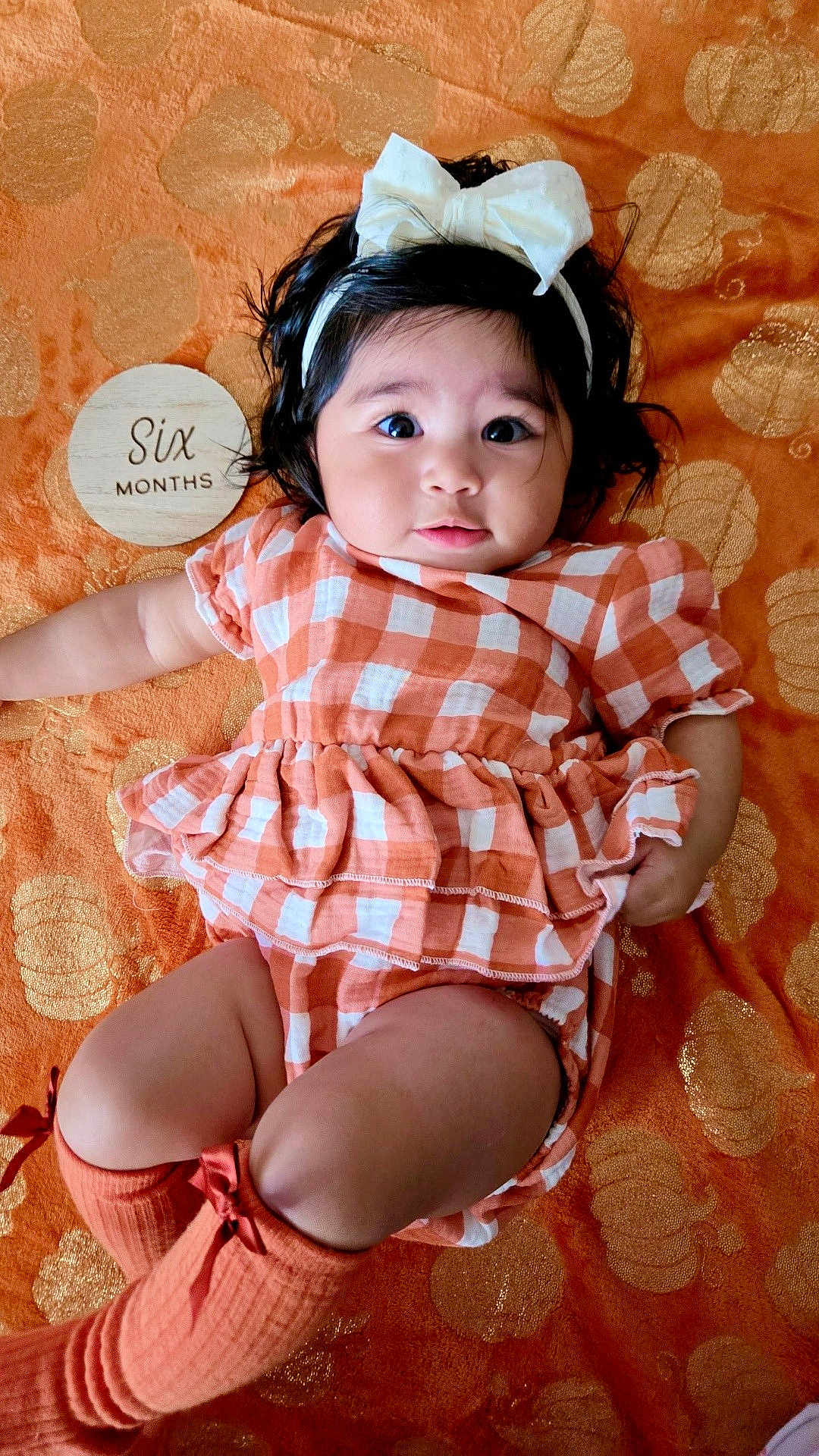 Zyla is registered to the contest to win money with this photo: baby, infant, child, girl, headband, bow, milestone, six_months, orange, checkered, outfit, socks, blanket, pattern, cute, lying_down, portrait, face, skin, expression