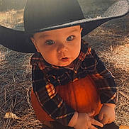 Rhyott is registered to the contest to win money with this photo: baby, child, cowboy_hat, pumpkin, plaid_shirt, outdoor, autumn, sunlight, nature, fall, grass, hands, cute, portrait, hat, person, seasonal, young_child, sitting, daylight