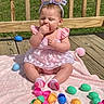 Ava is registered to the contest to win money with this photo: baby, child, bunny_ears, pink_dress, easter_eggs, plastic_eggs, blanket, outdoor, wooden_deck, grass, sunlight, sock, cute, closed_eyes, sitting, toy, headband, spring, holiday, playtime