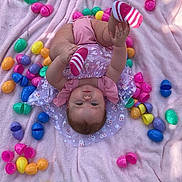 Ava is registered to the contest to win money with this photo: baby, infant, child, blanket, pink_blanket, easter_eggs, colorful_eggs, toy, outdoor, grass, playful, cute, smiling, clothing, striped_socks, reaching, lying_down, sunlight, happy, portrait