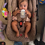 Eliana is registered to the contest to win money with this photo: baby, infant, child, car_seat, bottle, feeding, sitting, portrait, face, eyes, hair_bows, pink_clothing, toy, colorful_toy, indoor, tile_floor, family, safe, candid, photography