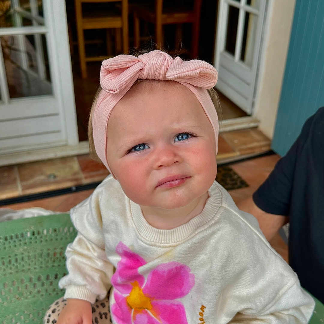 Love a rejoint le concours — aidez-le/la à gagner de superbes lots ! adult_hand, blue_eyes, child, curious, door, expression, flower_print, green_chair, hand, indoor, leggings, leopard_print, person, pink_headband, seated, socks, sweater, table, toddler, wooden_chair
