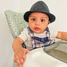 Khristine Spencer joined the competition — help win amazing prizes! baby, child, hat, fedora, high_chair, plaid, overalls, white_wall, cushion, indoor, person, cute, curious, hand, face, seated, infant, clothing, portrait, eyewear