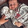 baby, smiling, child, onesie, puppy_print, blanket, hand, cloth, leather_couch, cozy, infant, cute, blue_eyes, soft_texture, portrait, lying_down, happy, indoor, close_up, skin