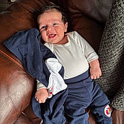 Hudson is registered to the contest to win money with this photo: baby, infant, smile, happy, clothing, onesie, pants, jacket, couch, leather, blanket, hand, foot, face, person, indoors, comfort, cozy, relaxing, child
