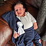 baby, infant, smile, happy, clothing, onesie, pants, jacket, couch, leather, blanket, hand, foot, face, person, indoors, comfort, cozy, relaxing, child