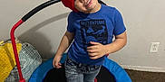 Jeremiah joined the competition — help win amazing prizes! child, red_hat, blue_tshirt, dinosaur_print, trampoline, barefoot, carpet, indoor, smiling, playful, head_tilt, jeans, toy, home, young_child, fun, leisure, room, blanket, cushion