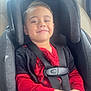 child, car_seat, boy, smiling, red_clothing, jeans, seatbelt, car_interior, happy, casual_wear, portrait, young_child, safety, seat, window, daylight, cute, hands, hair, face