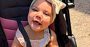 Rosalie joined the competition — help win amazing prizes! baby, child, smiling, stroller, headband, bow, sunlight, toy, yellow, happy, cute, outdoor, infant, seatbelt, clothing, person, portrait, babywearing, summer, playful