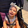 baby, child, smiling, stroller, headband, bow, sunlight, toy, yellow, happy, cute, outdoor, infant, seatbelt, clothing, person, portrait, babywearing, summer, playful