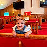 baby, bow, candle, child, church, cross, cute, denim, furniture, girl, happy, headband, interior, overalls, pew, red_carpet, religious, smile, television, wood_paneling