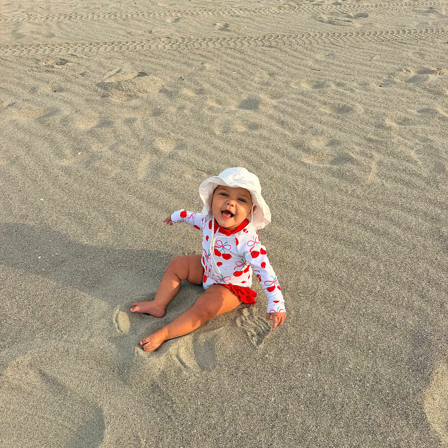 Rosalie joined the competition — help win amazing prizes! baby, child, beach, sand, ocean, waves, sunhat, swimsuit, sitting, happy, smiling, summer, outdoor, footprints, water, nature, playful, sunlight, vacation, holiday